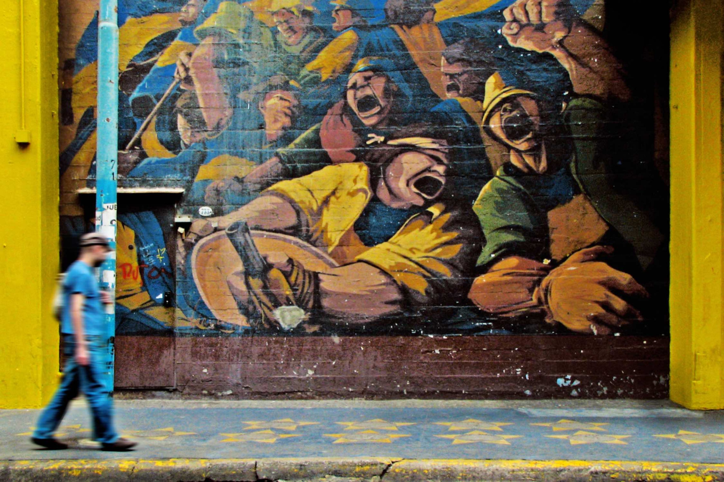 Image of man walking on the street in front of a wall of street art.