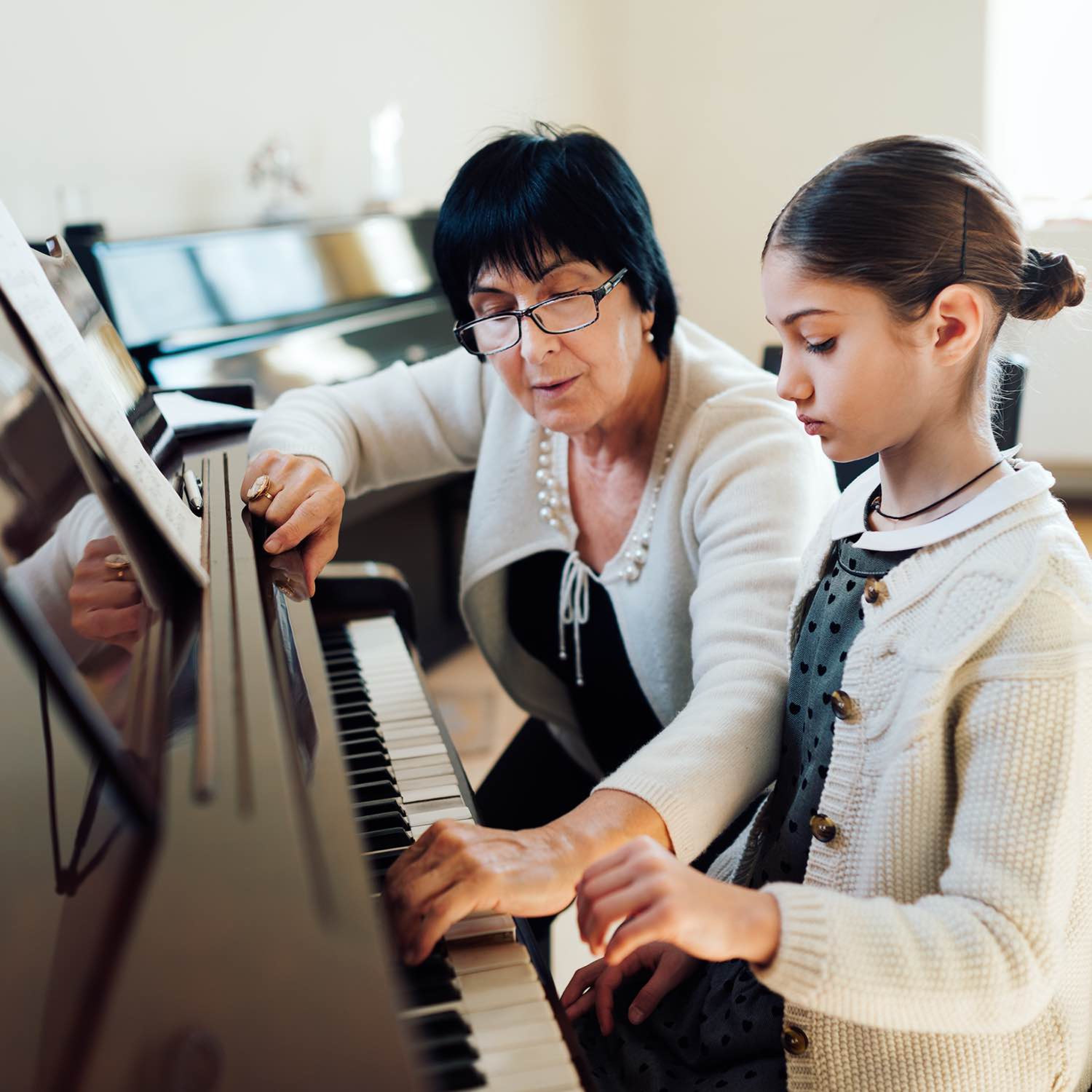 Young girl playing the piano with an instructor alongside her.