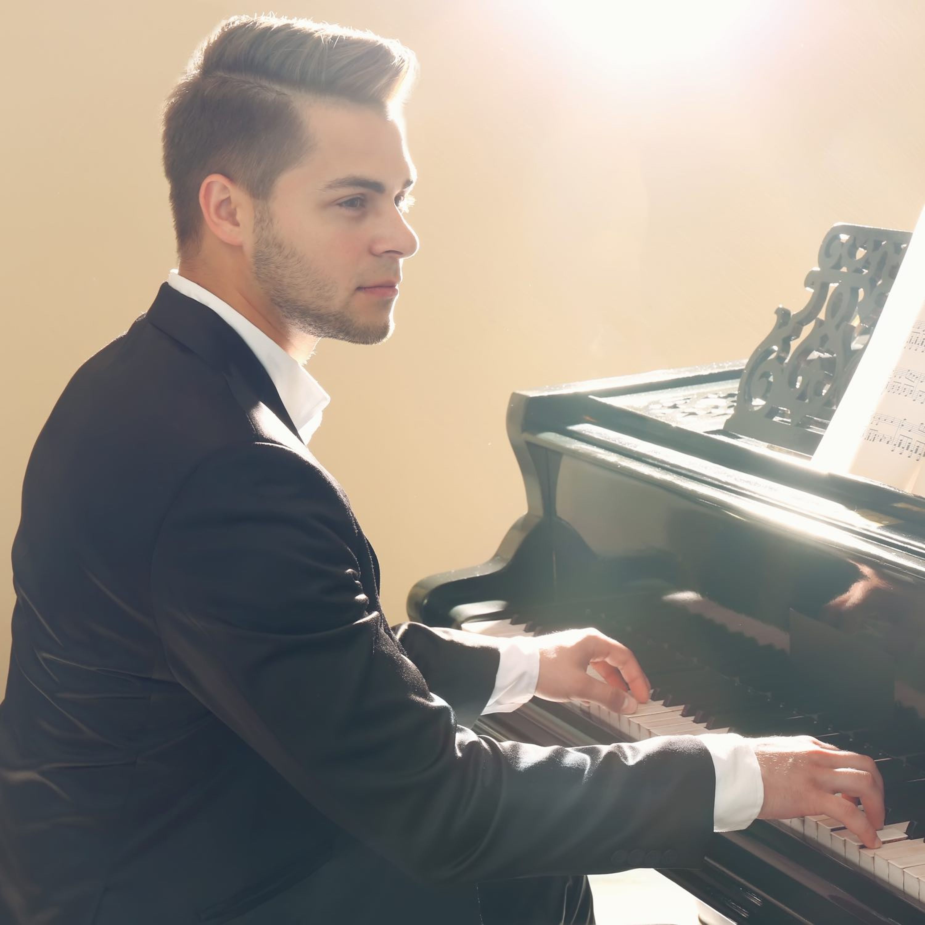 Man sitting at a piano playing while looking to the right.