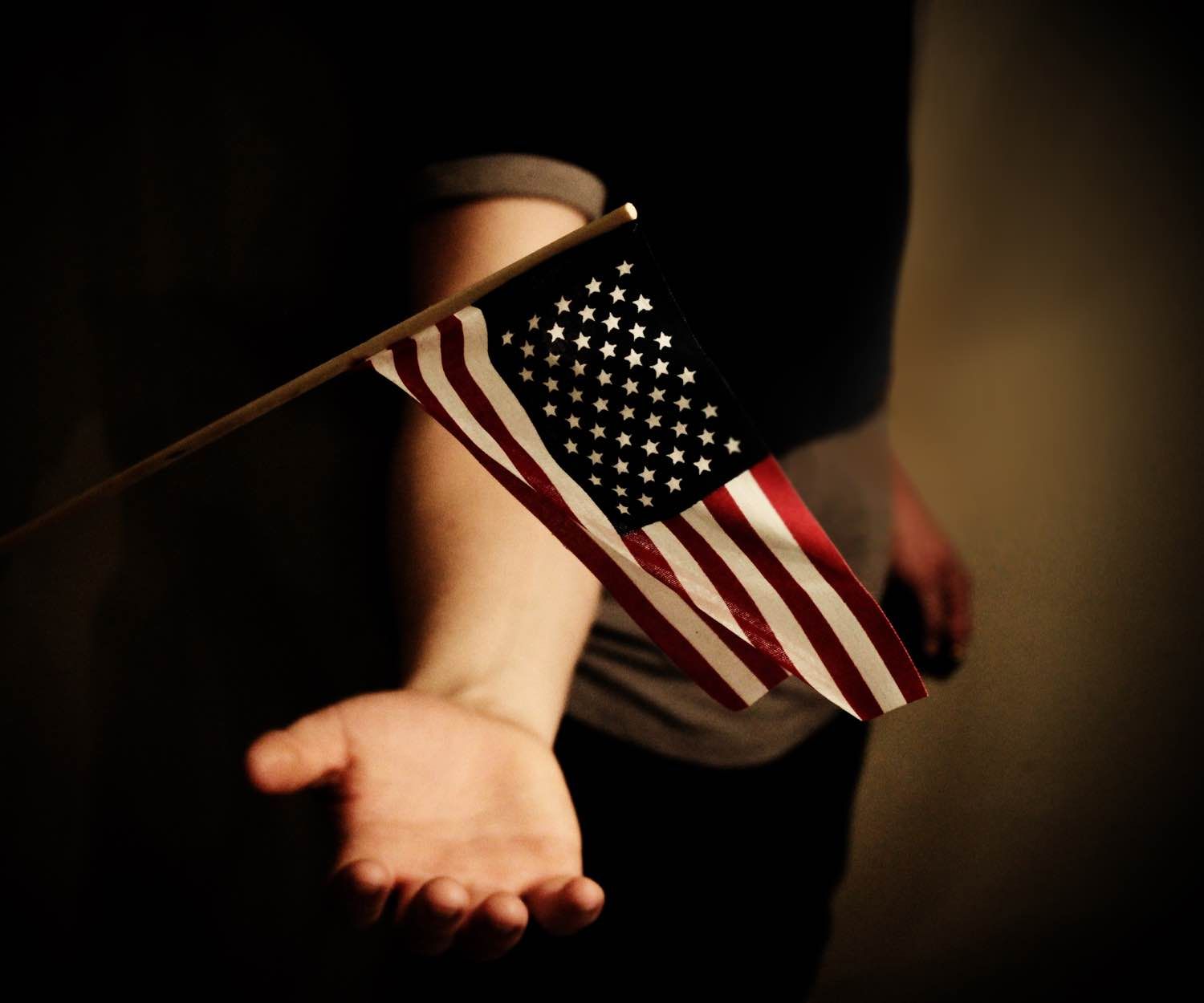 Image of a arm reaching out to a small American flag.