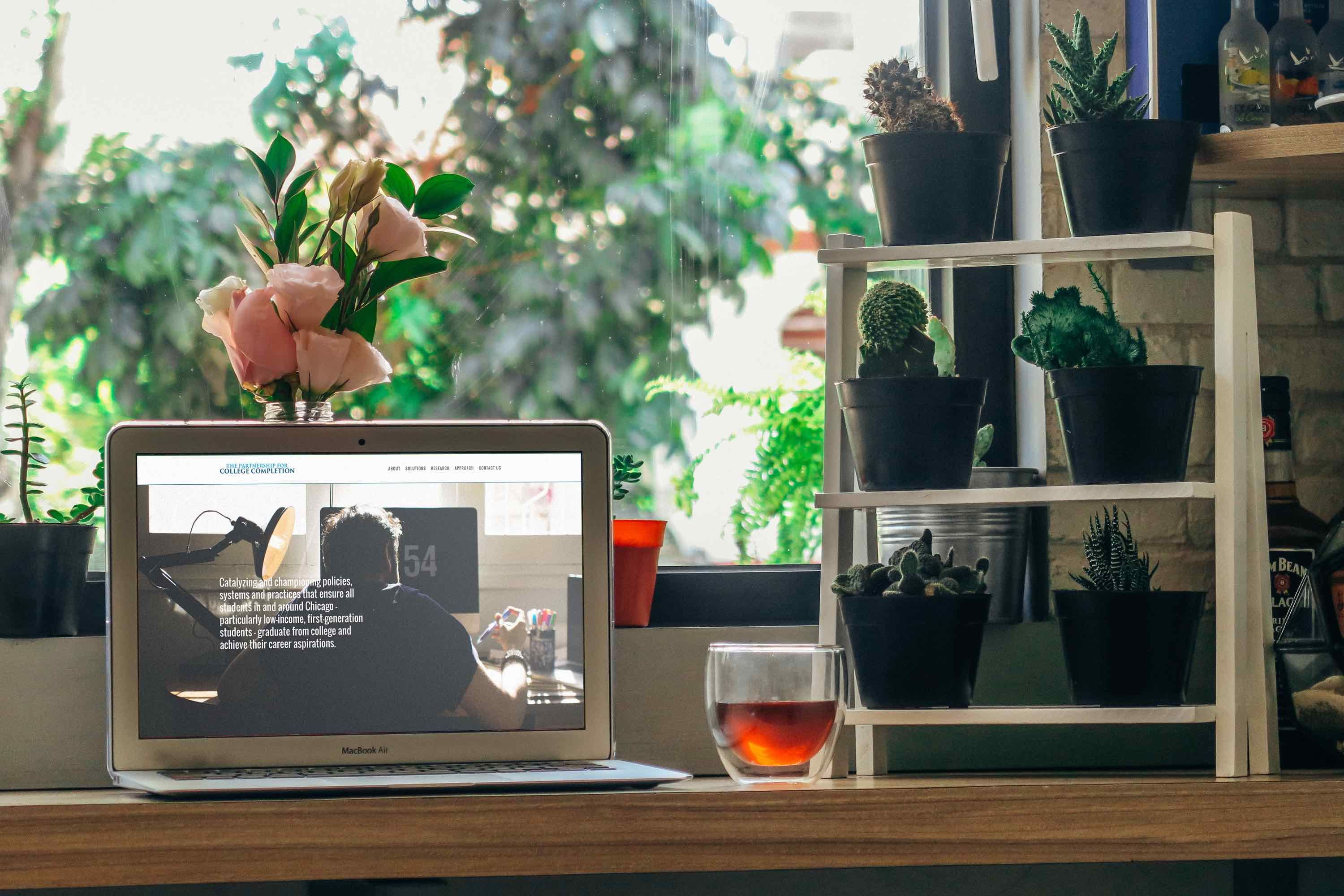 Image of a desk with a laptop computer on it and glass of wine.