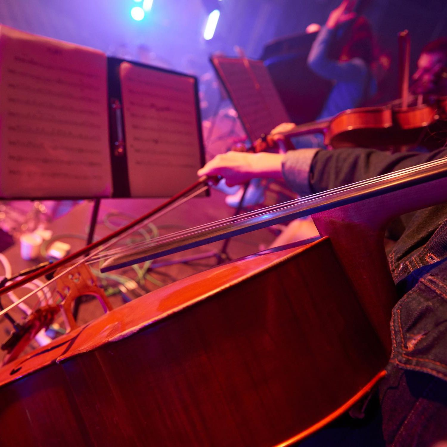 Image of people playing cellos and violins looking at a music stand.