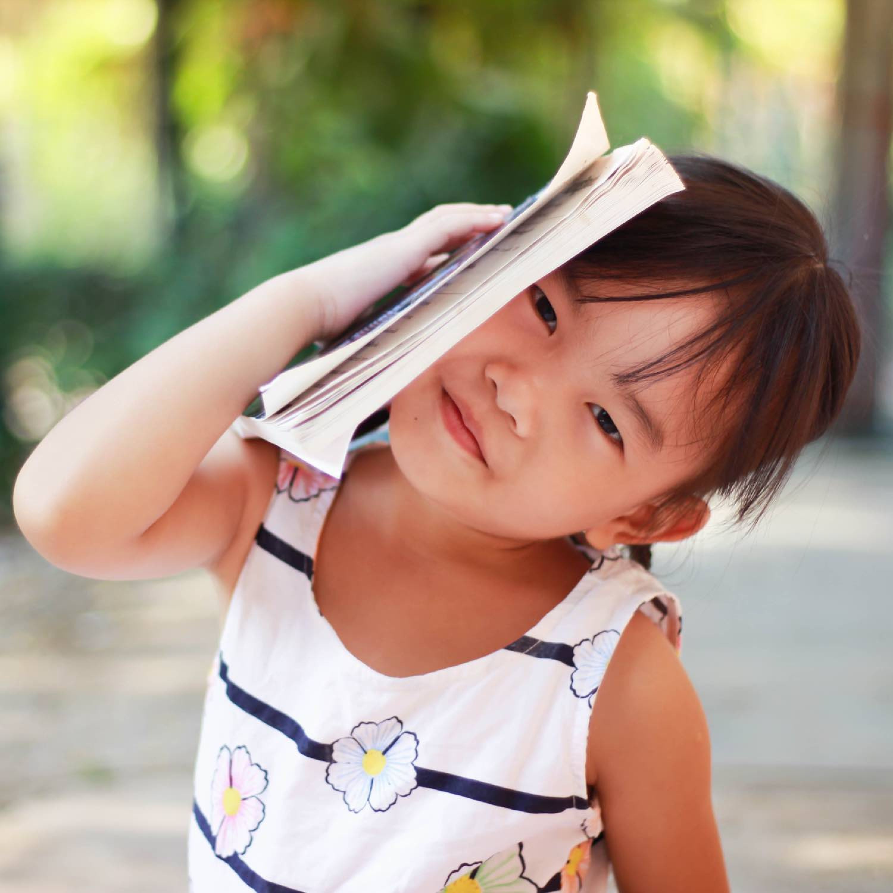 Image of a little girl holding a book to the side of her head.