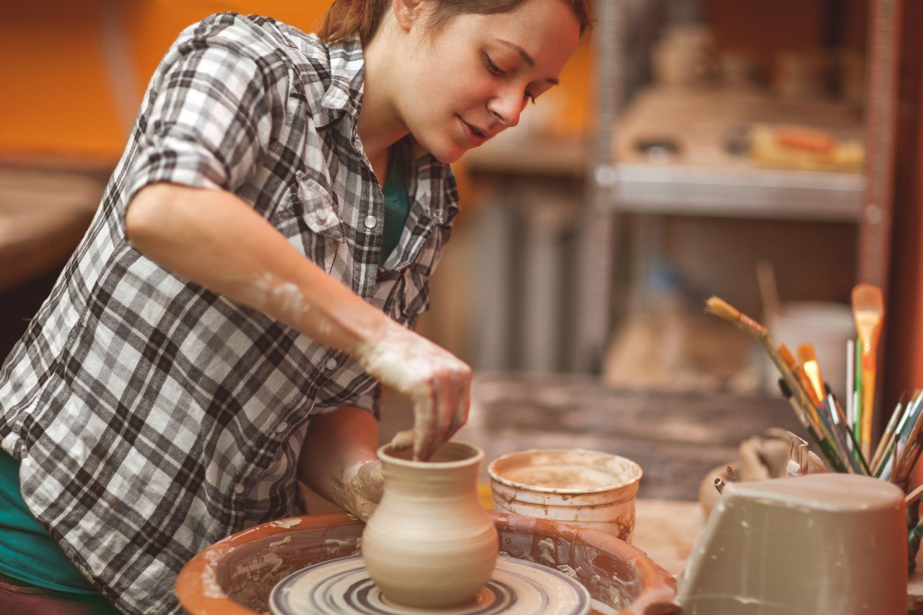 Woman potter and a spinning wheel creating a vase.