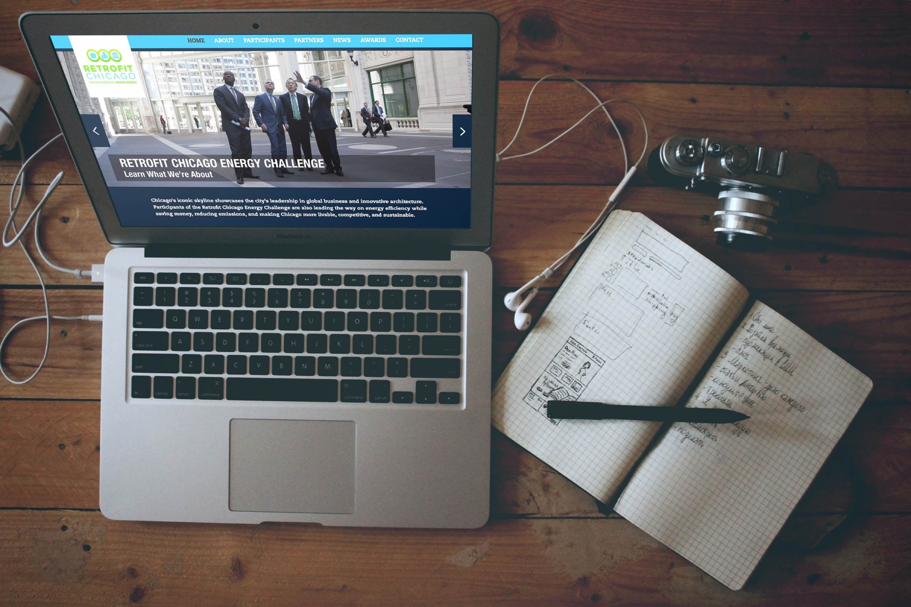 Image of an open laptop on a desk with a notebook and pen next to it.