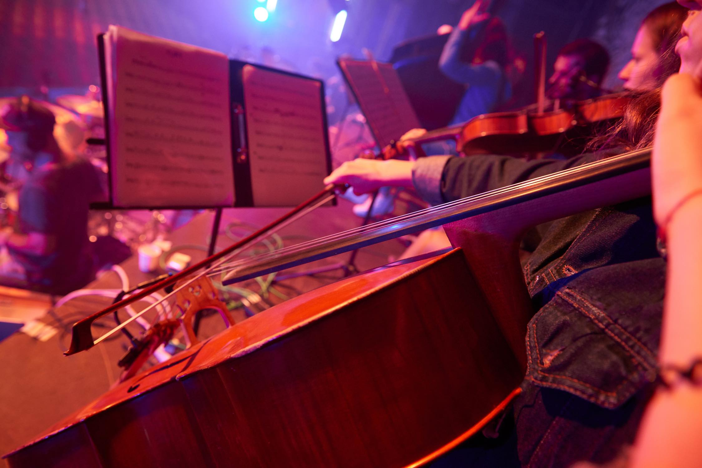 Image of people playing cellos and violins looking at a music stand.