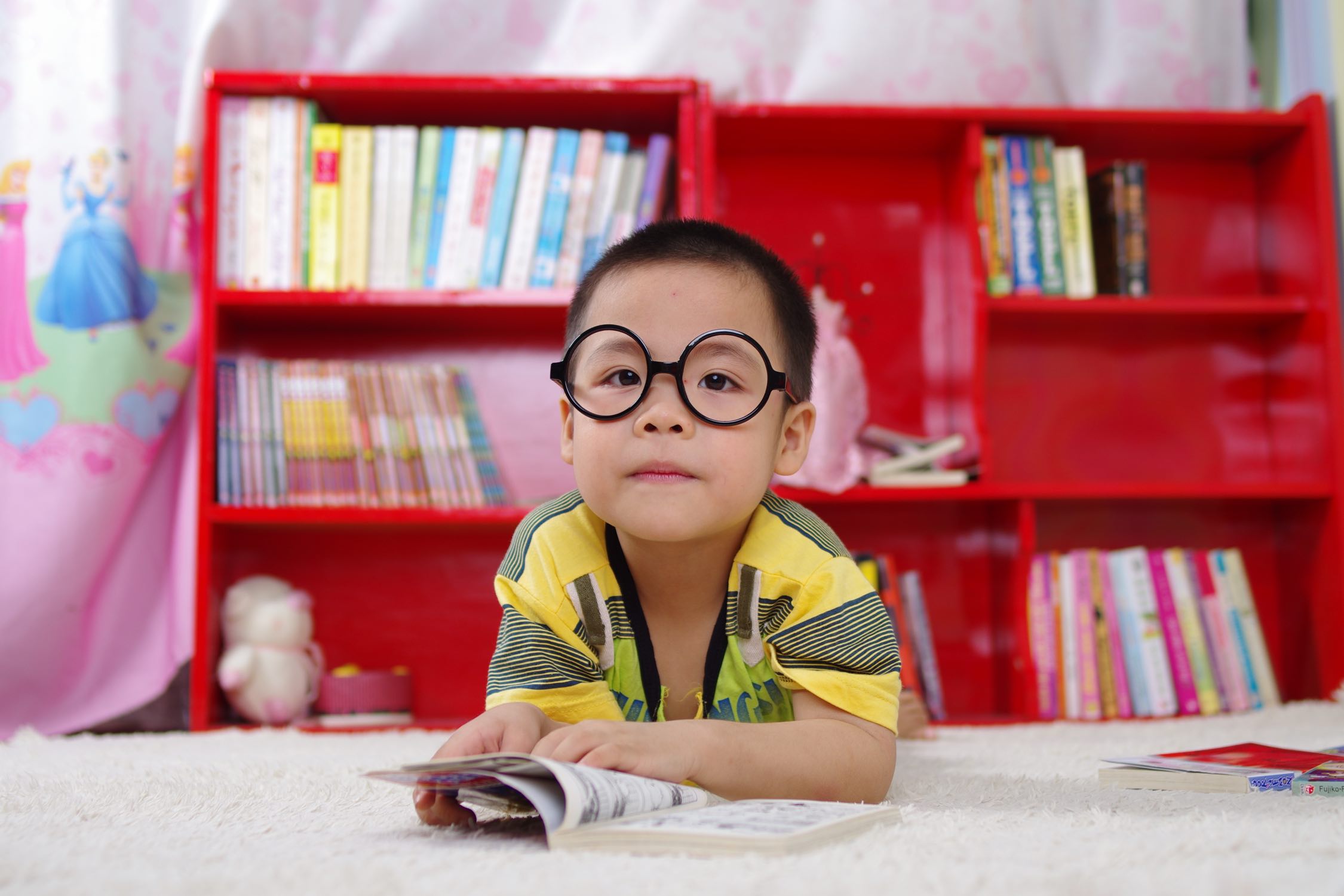 Image of little boy with big black round glasses reading a book.