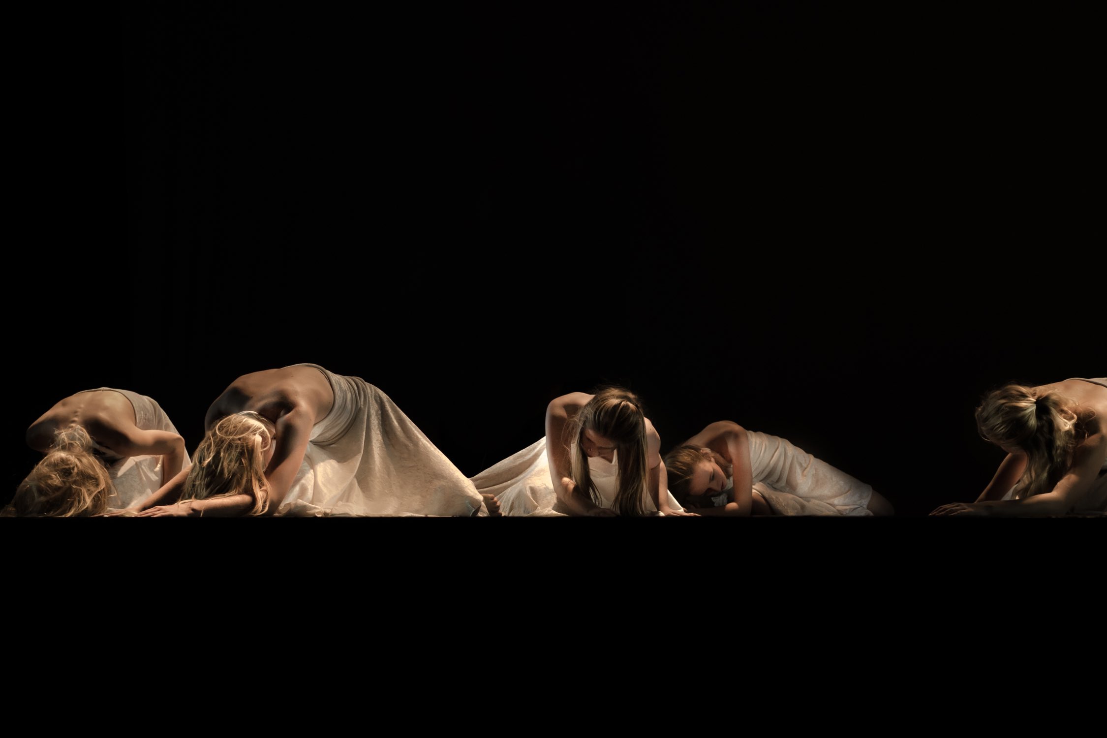 Image of multiple dancers crouched down on a stage.