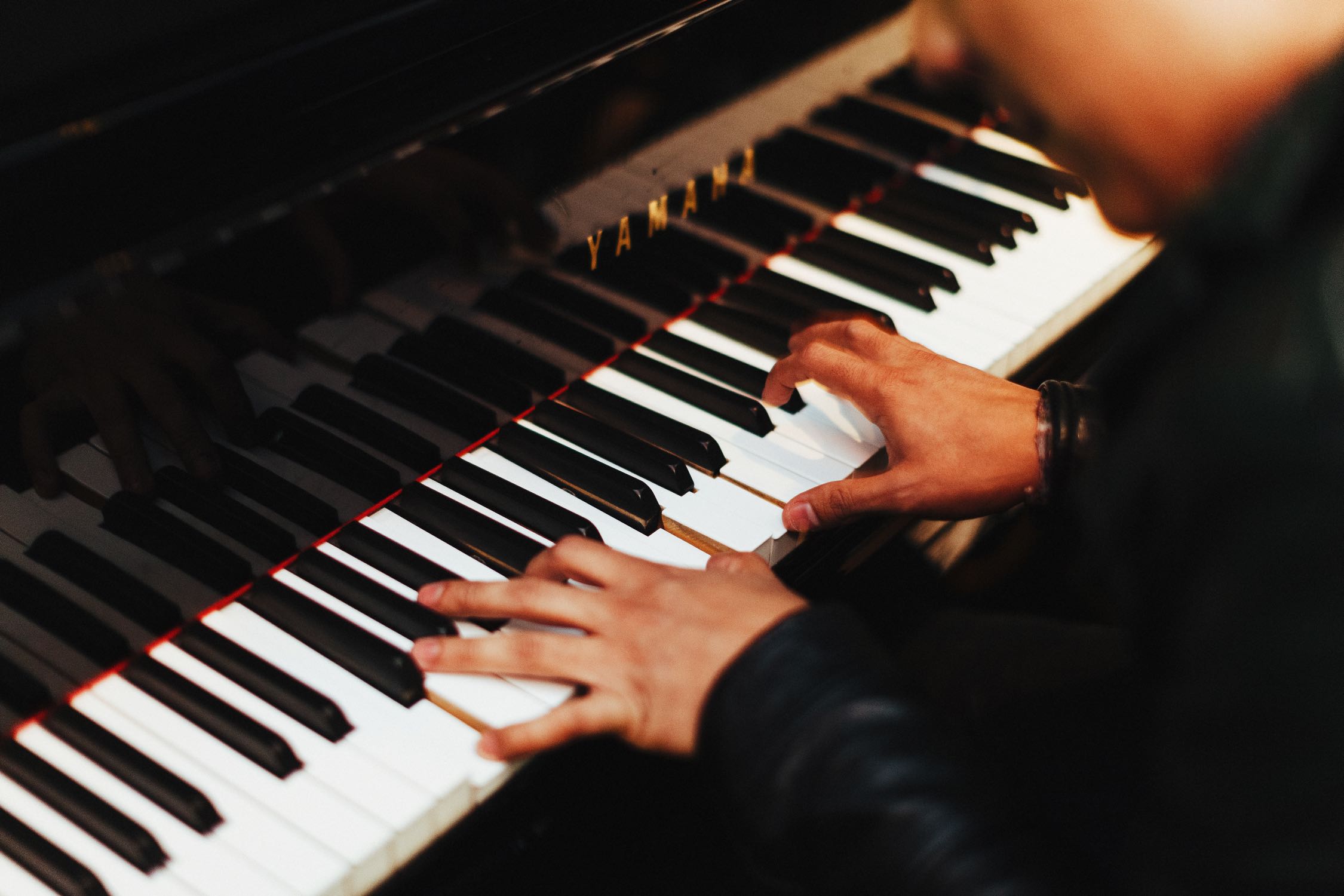 Hands playing a Yamaha piano.