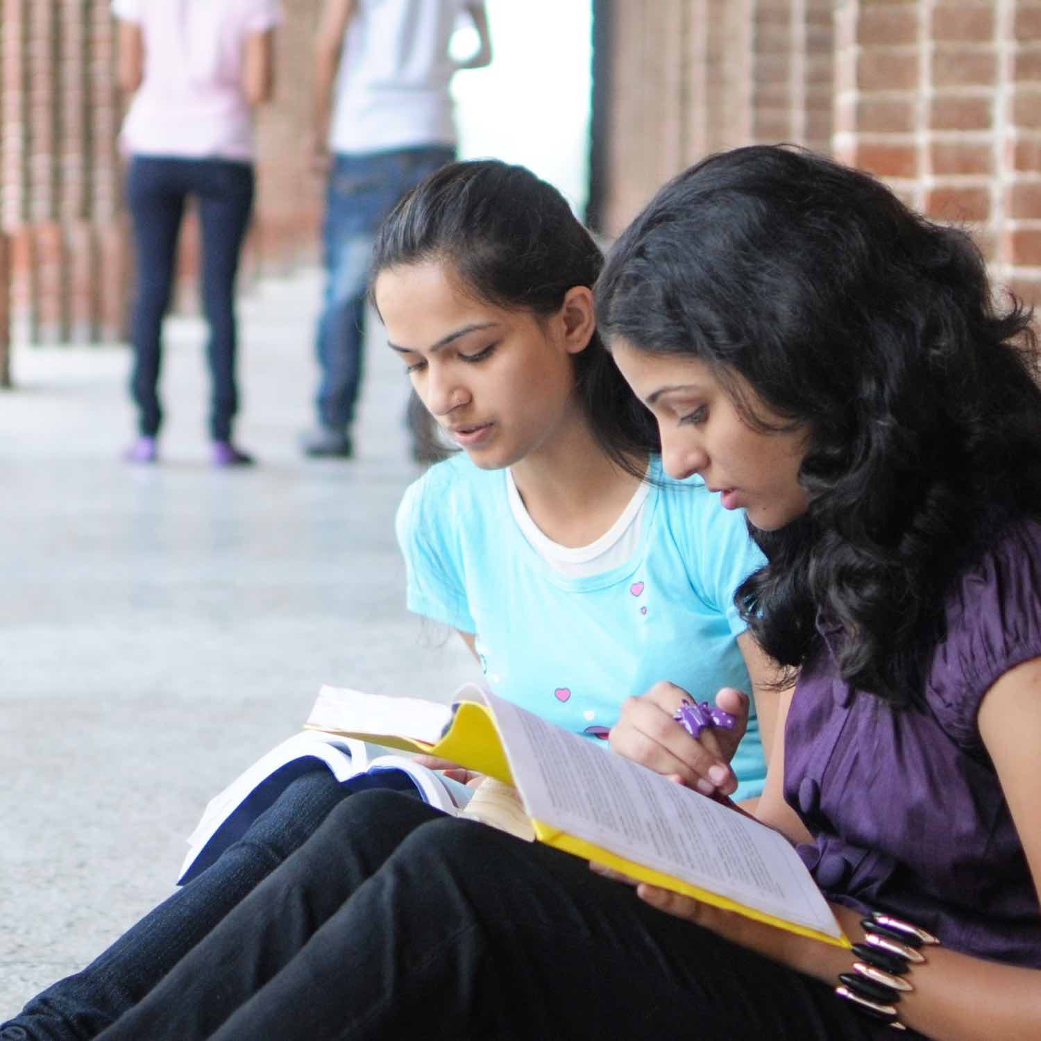 Two girls sitting and reading text books.